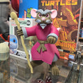 Action figure with pink and gray outfit in front of a Teenage Mutant Ninja Turtles book