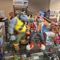 Two animated character figurines on a glass display case with various items in the background.