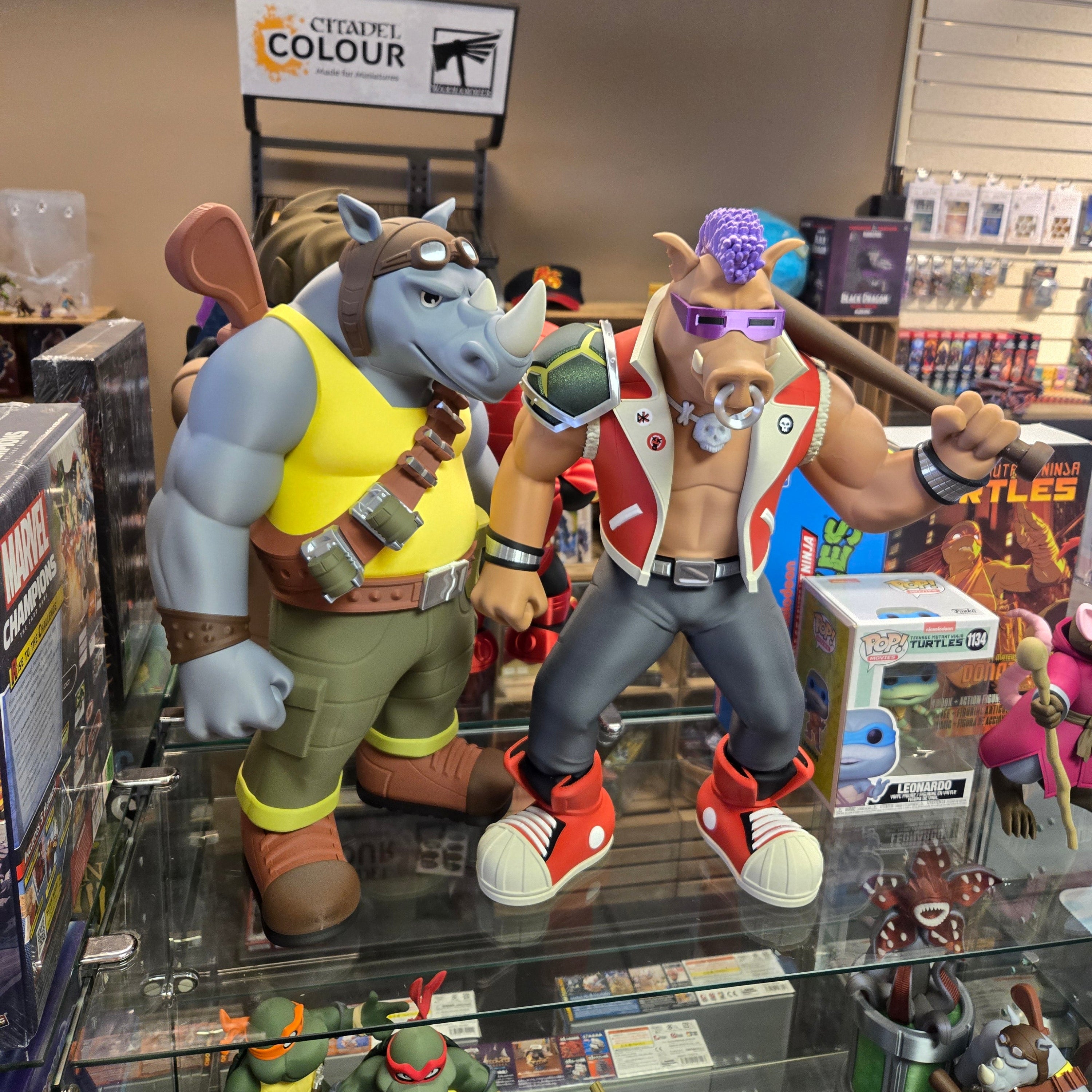 Two animated character figurines on a glass display case with various items in the background.