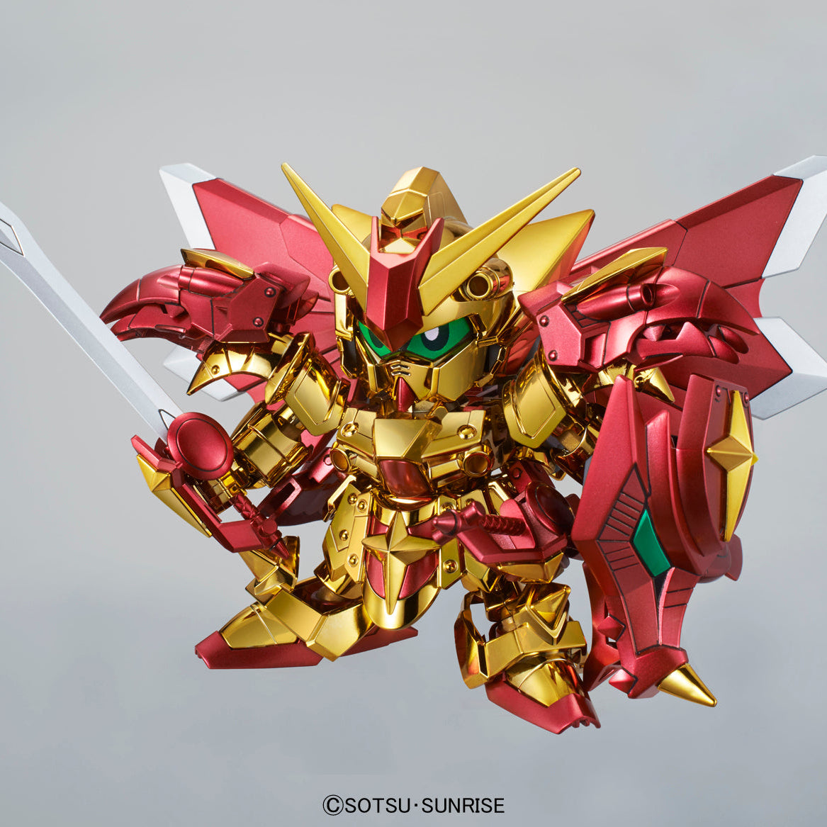 Gold and red mecha figurine holding a white sword, shown against a plain light gray background. A copyright mark for SOTSU-SUNRISE is visible at the bottom.