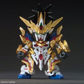 A small-scale collectible model of a Gundam-style mecha in metallic gold, white, blue, and red armor, photographed against a dark gray studio background. A copyright watermark for SOTSU-SUNRISE is visible in the bottom-left corner.