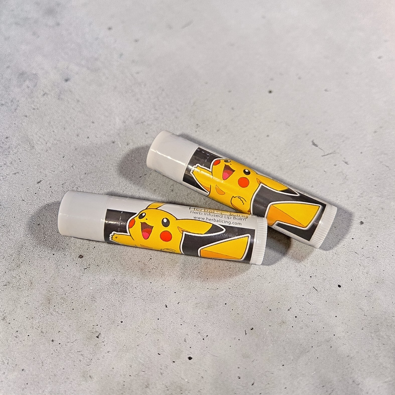 Two lip balms with Pikachu design on a gray surface