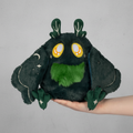 Plush toy resembling a black creature with green accents held by a hand on a white background