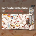 A product display for a 'Soft Textured Surface' playmat featuring a dense illustration of cute, smiling white fluffy creatures. The main playmat is shown flat, with its retail packaging standing to the right.