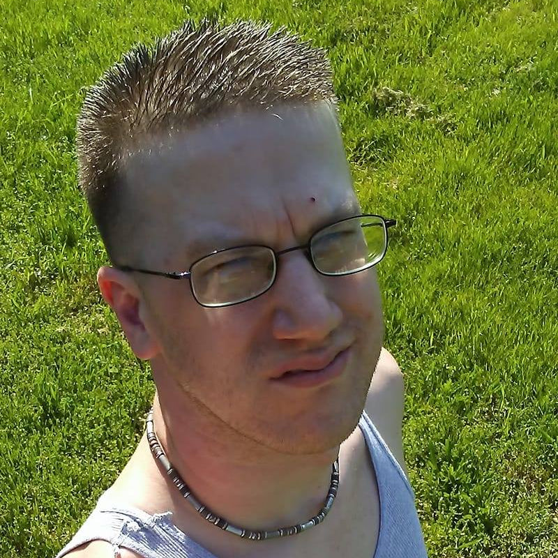 Person wearing glasses and a necklace standing on grass