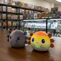 Two plush toys, one gray with black hair and one multicolored with orange hair, on a white background.