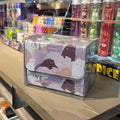 A clear plastic box containing a stack of dice bags with a dark cat pattern, displayed on a wooden counter inside a retail store.