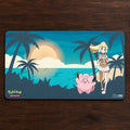 Pokémon-themed playmat with a character and a pink creature on a tropical background